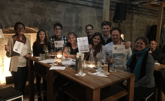 A group of past graduates in a bar holding mini university flags