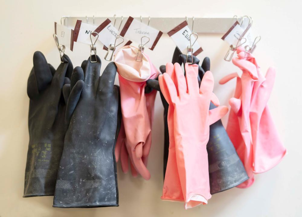 A row of rubber gloves hanging on a wall to dry, each labelled with a name.