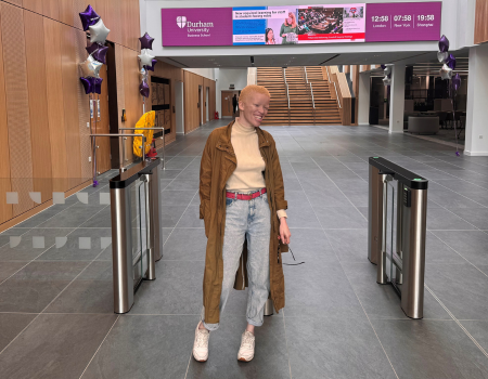Student in business school hallway smiling with news signs above her