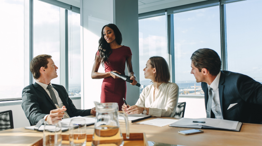 A businesswoman stands and addresses three seated male colleagues at a table