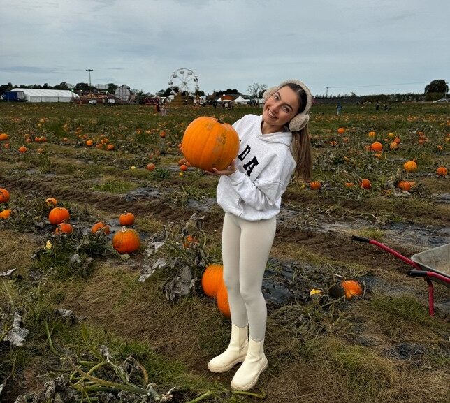 A student holding a pumpkin in a pumpkin field