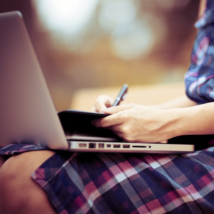 A student writing on a laptop and in a notepad