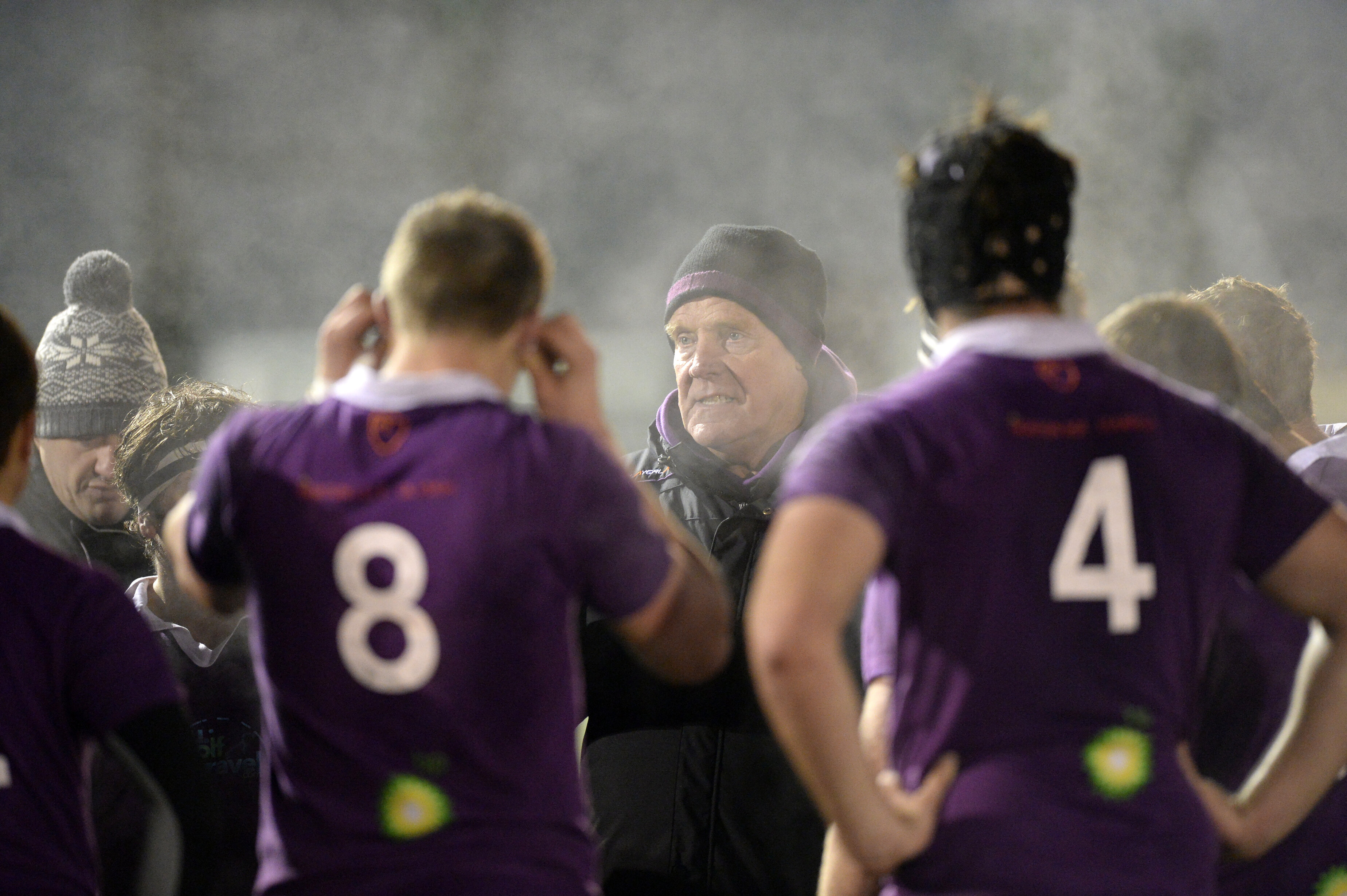 A huddle of purple shirted rugby players with coaches