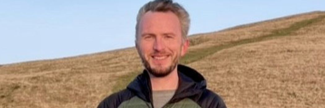 Joseph D Martin smiles at camera standing in the countryside