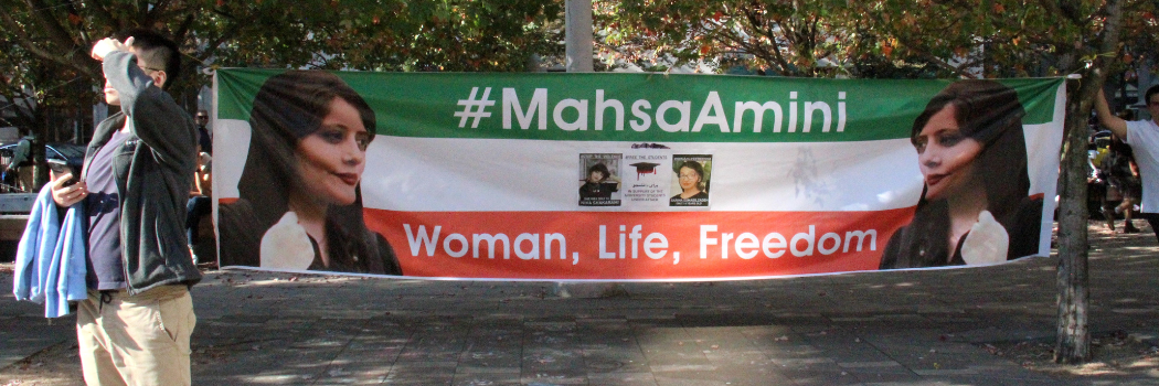 Two people standing by a banner which says #MahsaAmini - Woman, Life, Freedom