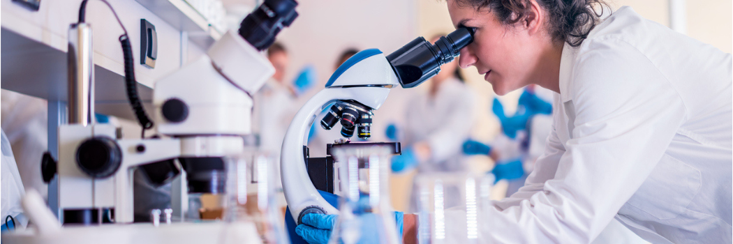 A young female scientist in a lab coat looking through a stethoscope.