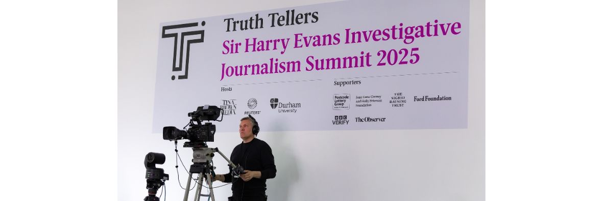 A video camera operator, with camera, stood in front of a large sign for the Truth Tellers summit