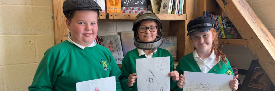 Three young people smile at the camera holding drawings they have made of rocket ships