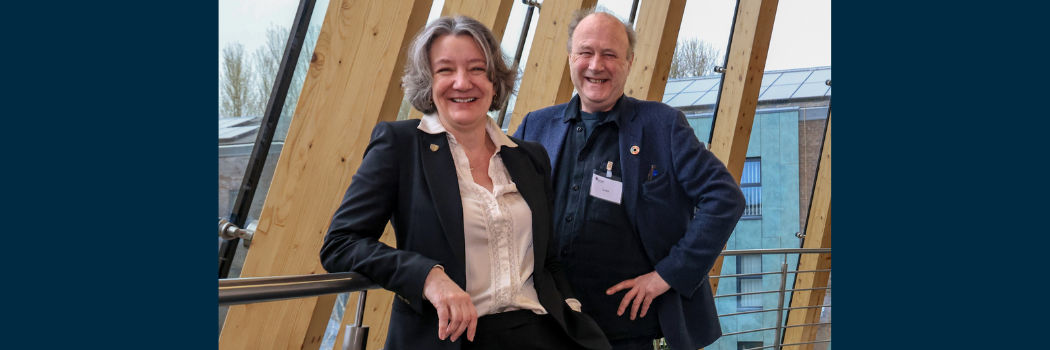 Female and male adults smiling with wooden framework of building in background