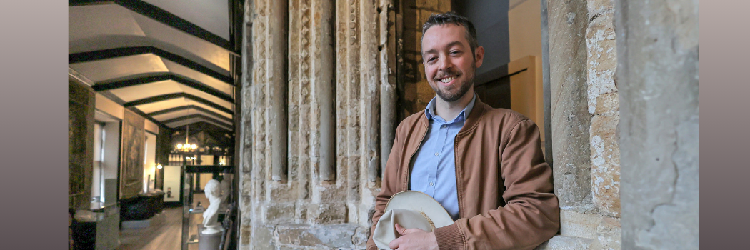 Waylon Cunningham standing in a corridor of Castle College with a smile on his face and holding a hat