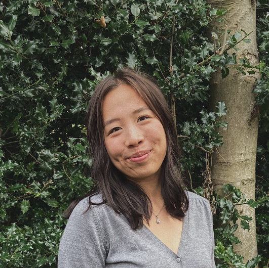 Student standing in front of green bushes