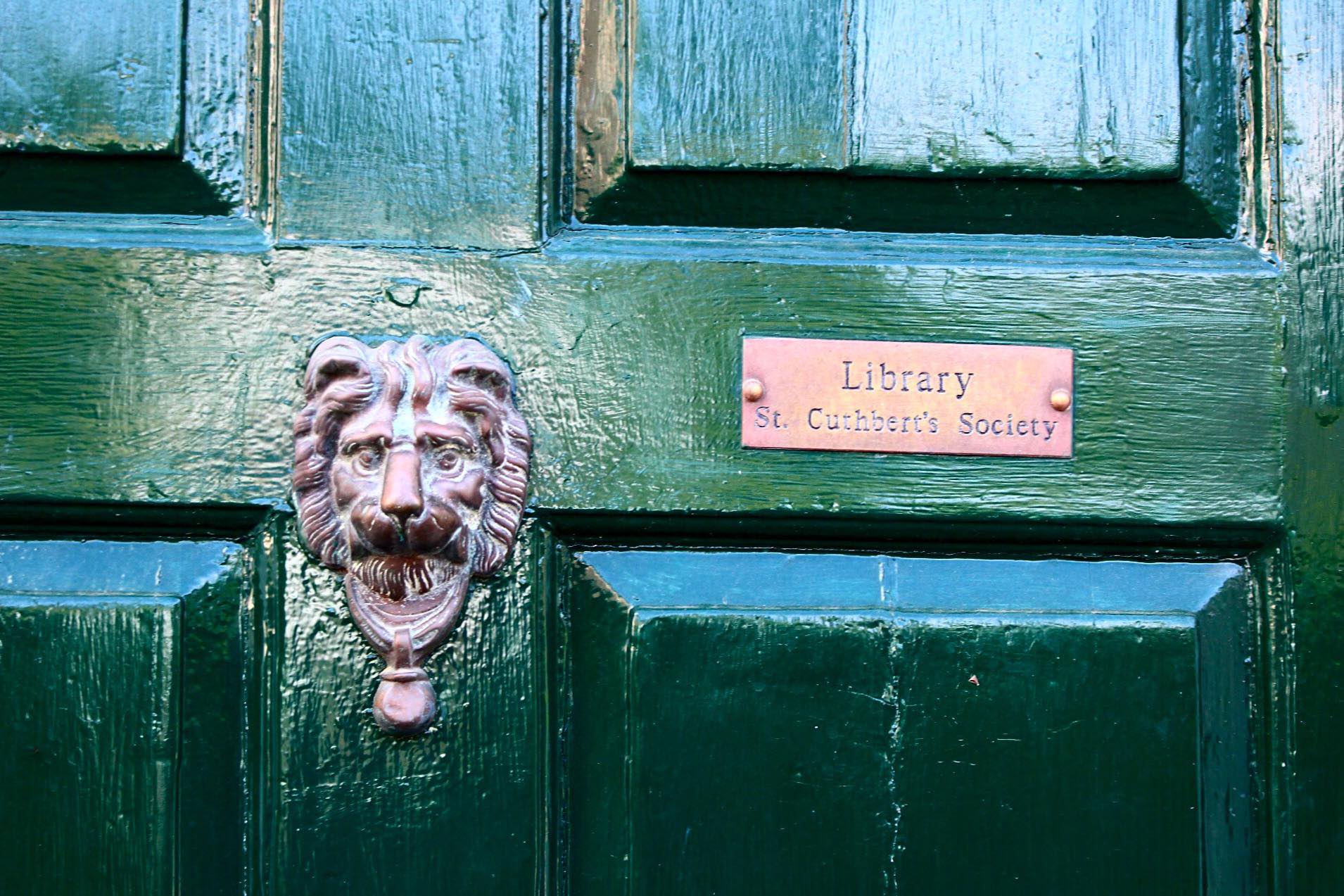 Dark green glossy wooden door with a lion knocker and St Cuthbert's Society Library plaque