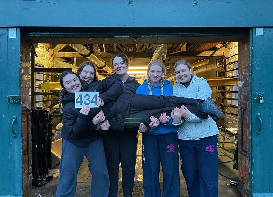 4 rowers in front of the boathouse holding their cox after winning a race