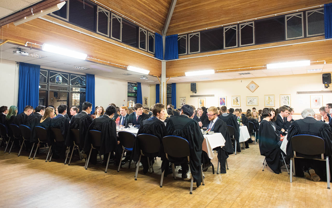 Students wearing black robes seated around tables in the hall