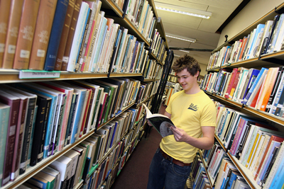 A student browsing the packed bookcases in our library