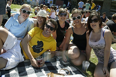 Students sitting on a picnic blanket laugh and smile as they enjoy the Jam by the Lake music festival on the college grounds
