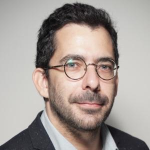 Rui Coelho smiling at the camera. He wears glasses and has a light grey background behind him.