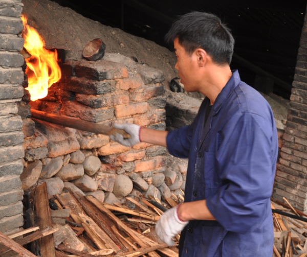 The kiln master feeds wood into the dragon kiln through the fuel holes located on its two sides to ensure a stable firing temperature. This experimental firing takes place in Longquan County, Zhejiang Province, in southern China. Photograph by Ran Zhang (2012)