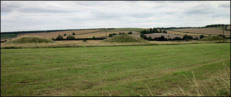 Two burial mounds in a field with hills in the background