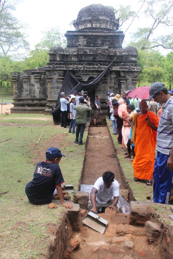 Religious monument in the background with visitors viewing an archaeological excavation underway in the foreground