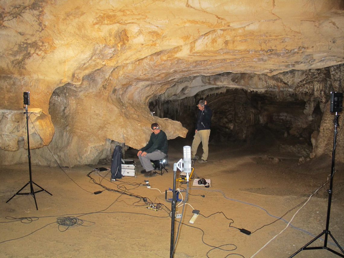 Two archaeologists within a cave with specialist sound measurement equipment including several tripods and cables trailing across the floor
