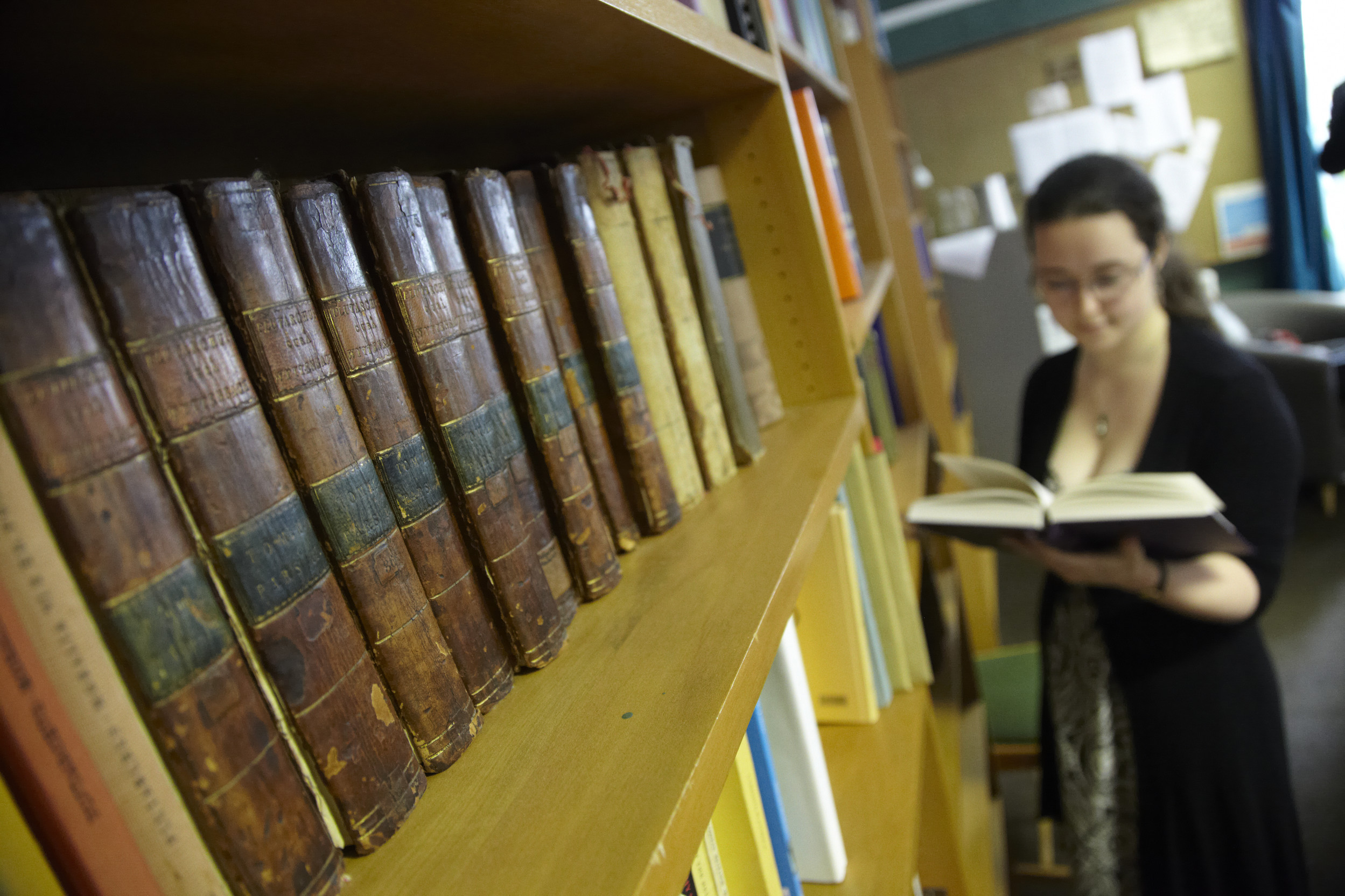 A student reading in the library, by a shelf of historic texts