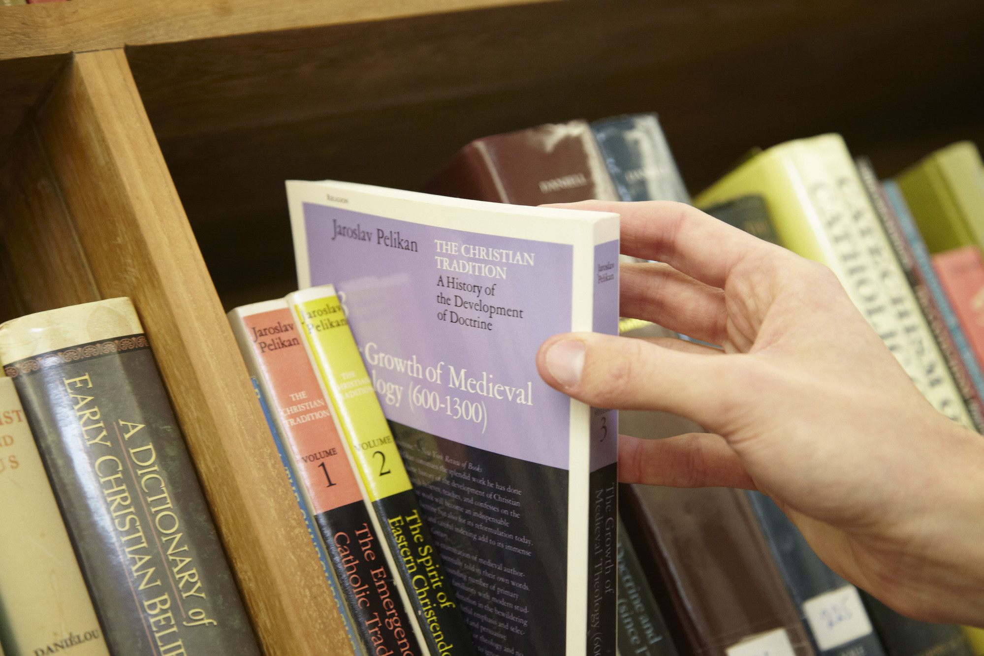 Person taking Theology book off a shelf close-up