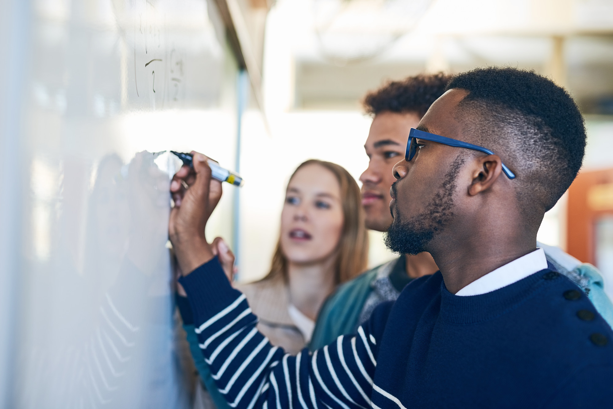 Person writing on a whiteboard while other people look on