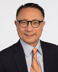 Rafael Macatangay smiling, wearing a suit, blue shirt and yellow striped tie