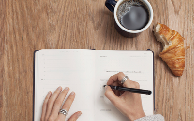 A person writing in a notebook with a cup of coffee