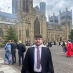 Graduate standing in front of Durham Cathedral