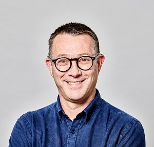 A man wearing glasses and smiling with a plain backdrop