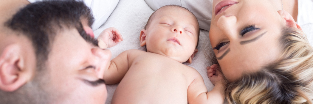 A man and woman on a bed with a sleeping baby in between them