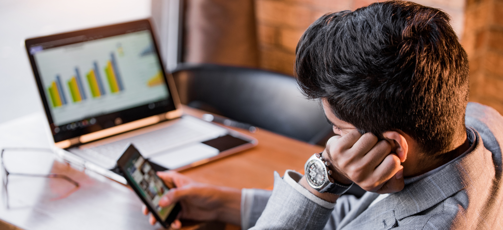 Man scrolling on phone in front of laptop