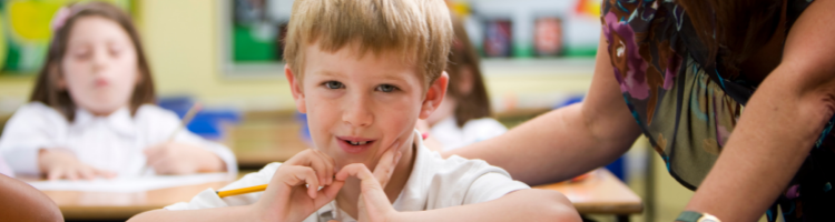 Young child sat at a desk with a teacher looking on