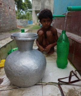 Child in Bangledesh sat with a water urn and green bottle