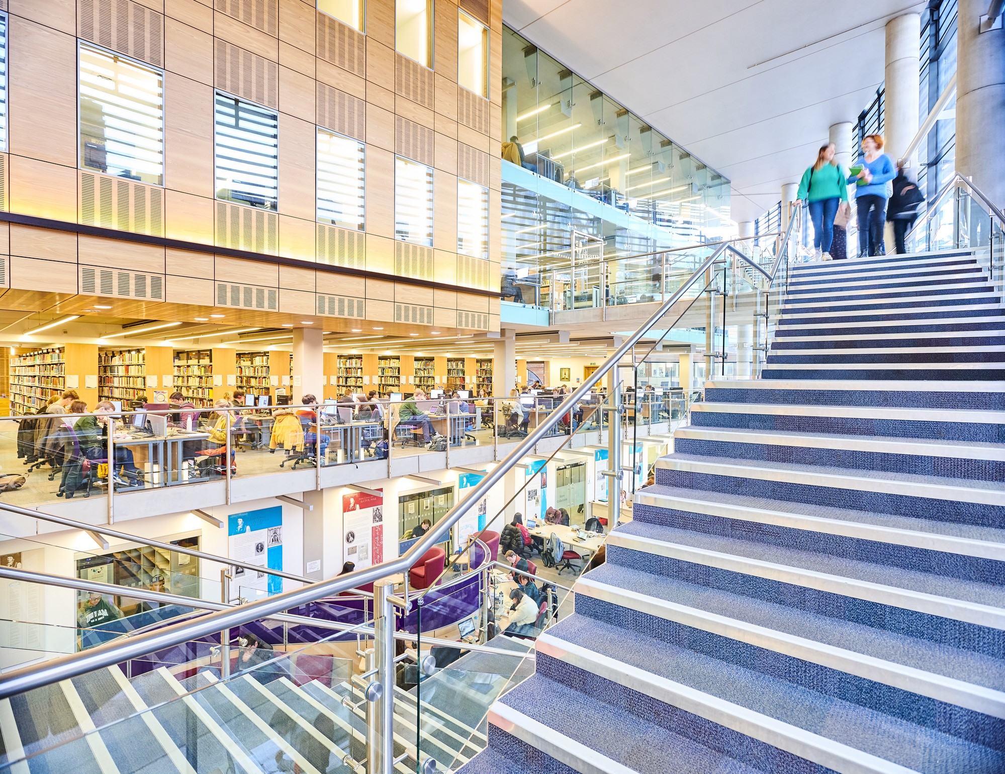 Students walking down stairs in library, bookshelves in the background