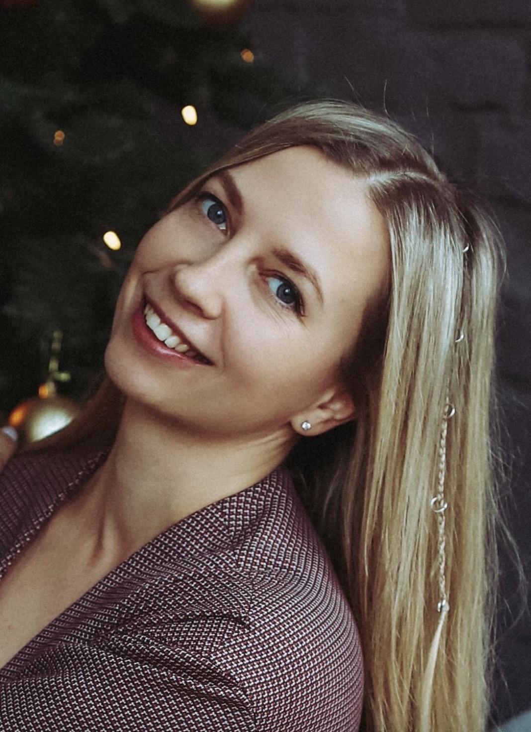 Portrait of a white female with long blonde hair and a purple, patterned shirt with a dark and sparkly background