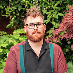 A man with a beard standing in front of a garden