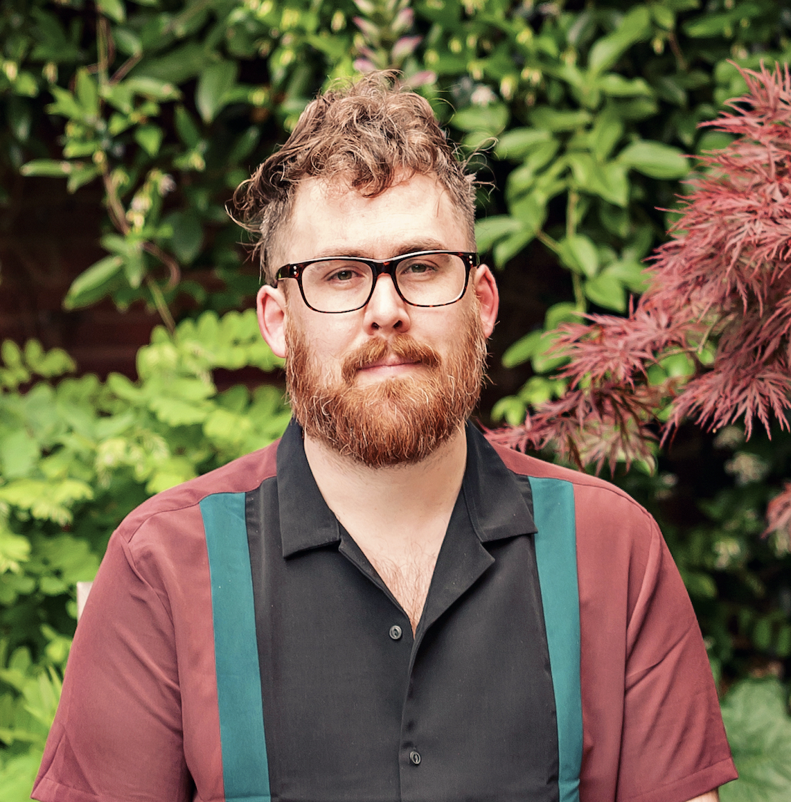 A man with a beard in front of a garden