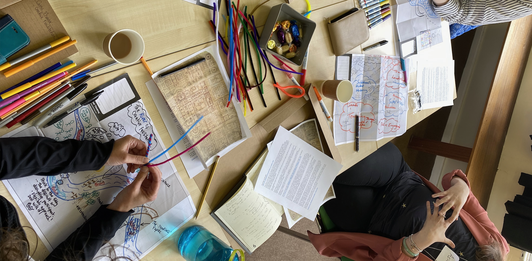 A close up of items on a table including pens, coloured pipe cleaners, imagery