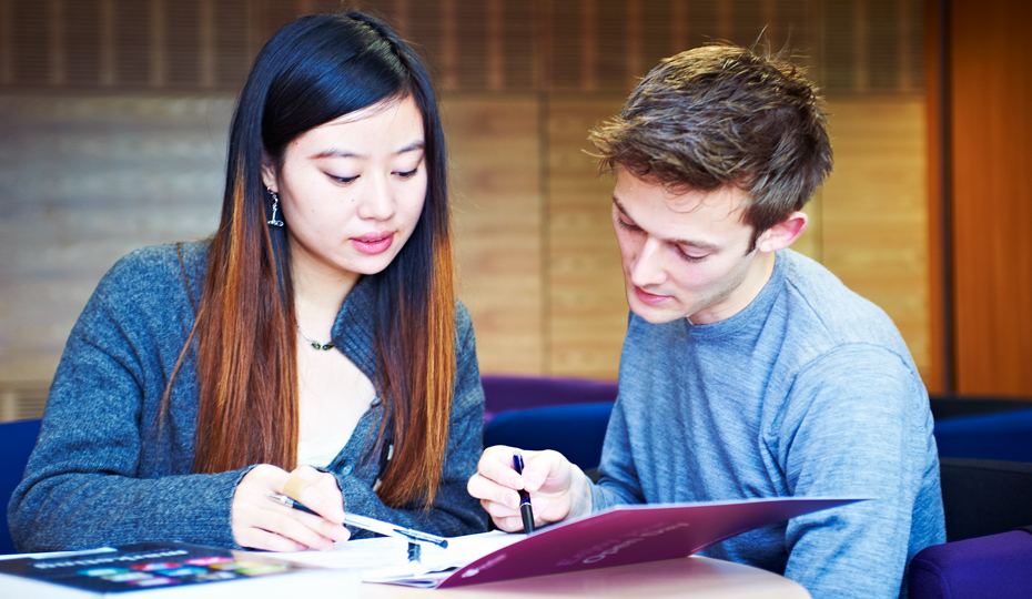 Two students working together over open academic textbooks