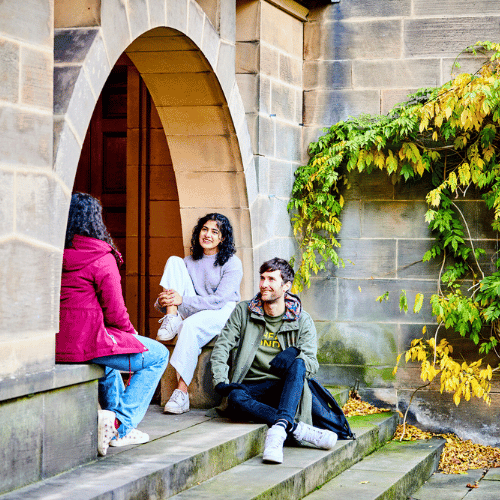 Three students sat chatting on the floor of a doorway.