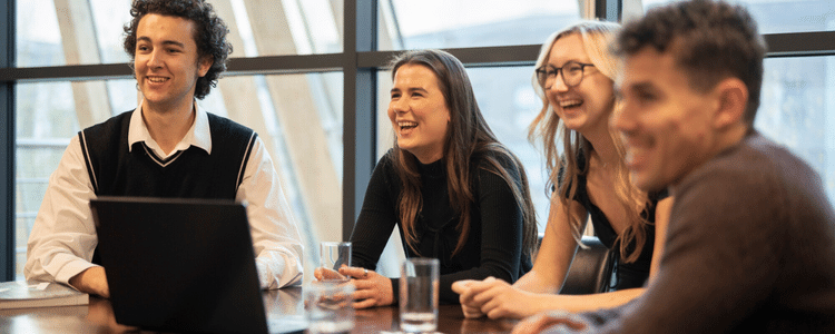 Four students laughing at a table with laptop