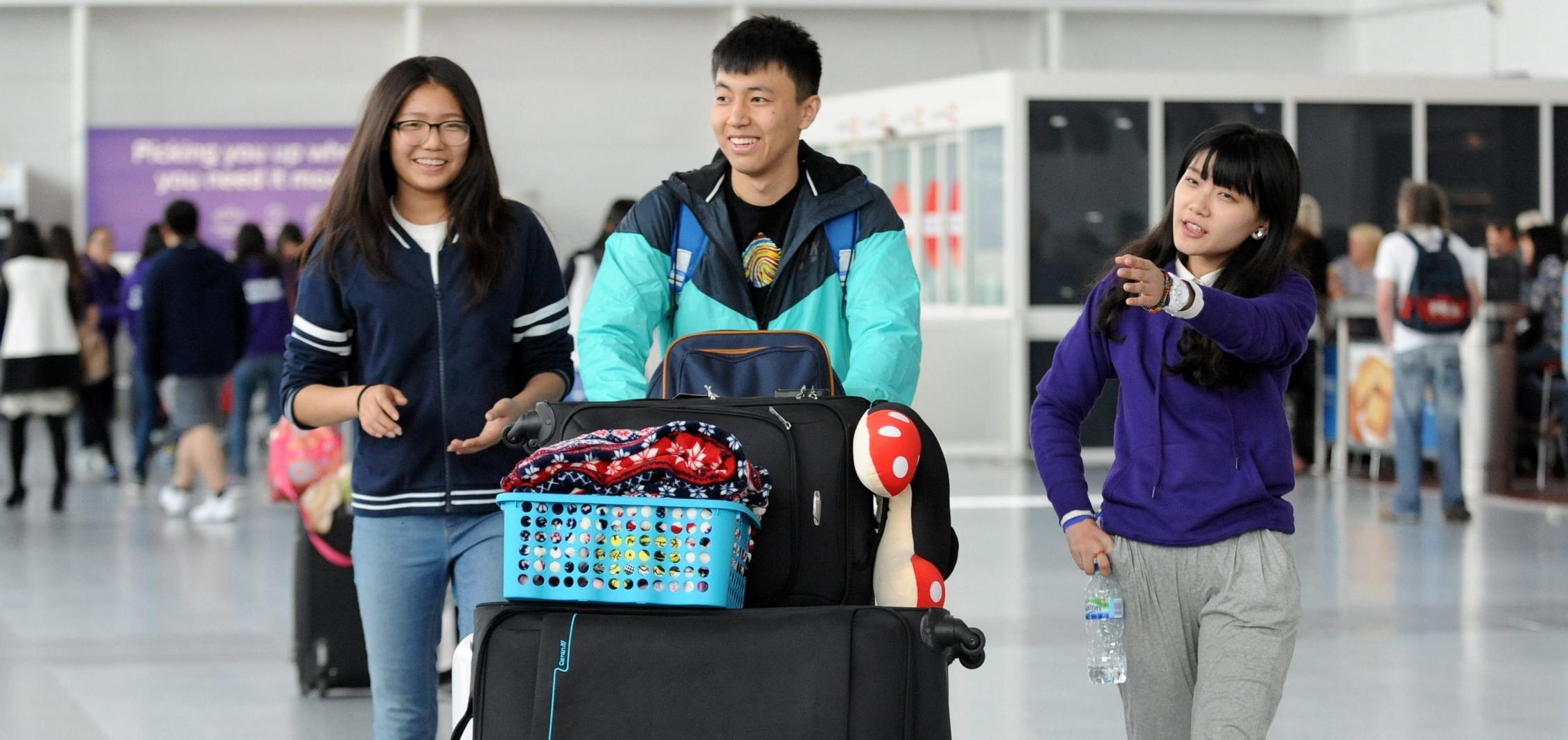 3 international students walking through Newcastle aiport cropped (1)