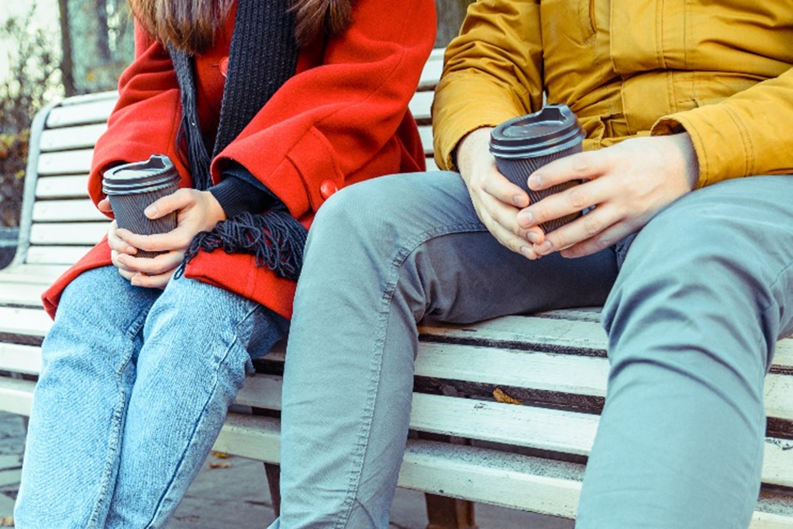 two students sitting on a bench holding cups of coffee