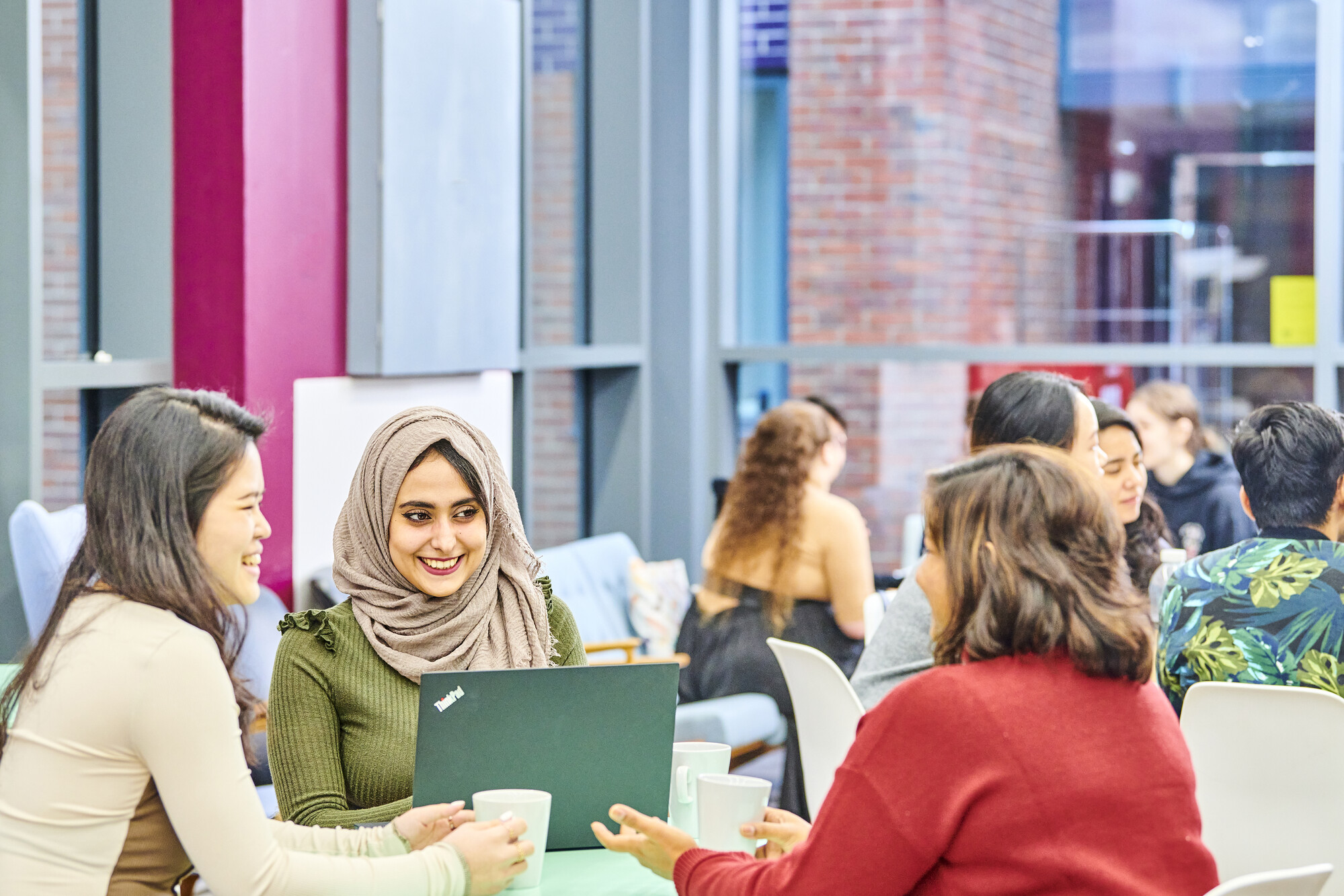 Group of postgraduate students smiling around a laptop with mugs