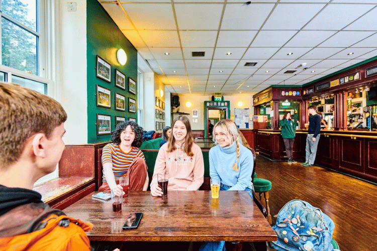 A group of students chatting around a table inside a student bar