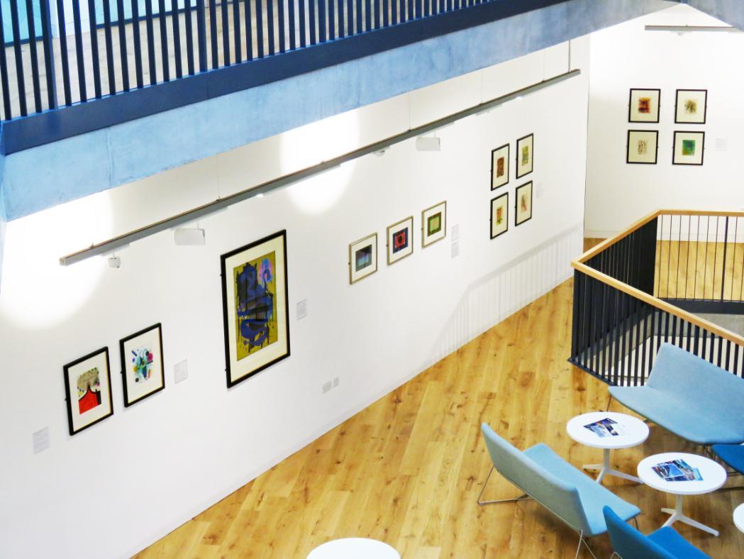 Ten artworks are displayed on a white wall, photographed from above.