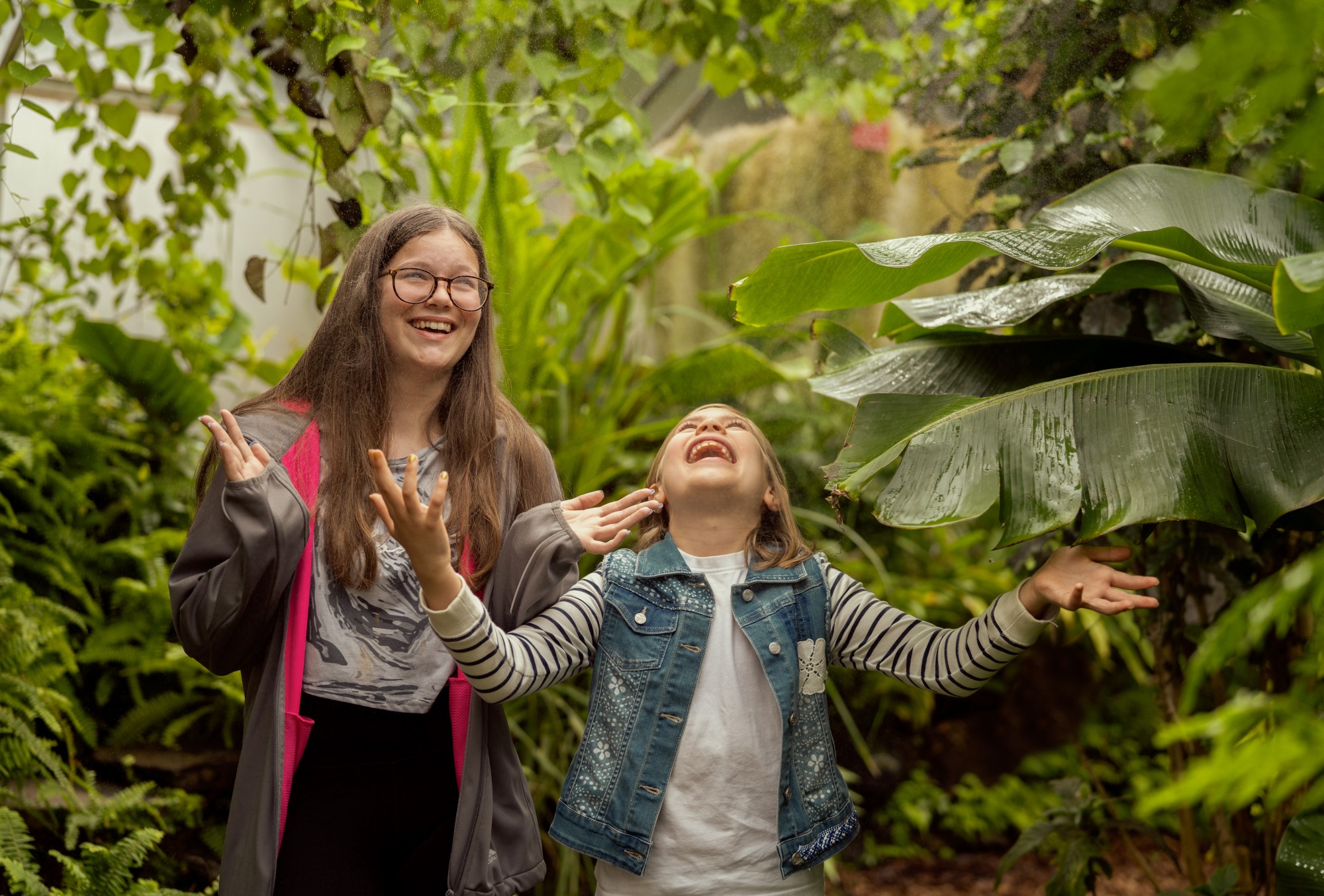 Two children enjoying the artificial rain in the Botanic Garden Greenhouse.